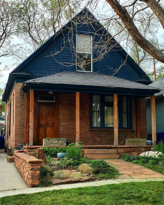 Charming old home with brick exterior, wooden porch, and landscaped front yard featuring greenery and stone walkway.
