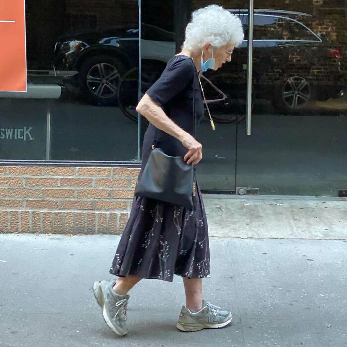 Elegant stylish grandparent walking on the street, wearing a flowy skirt, black top, crossbody bag, and casual sneakers.