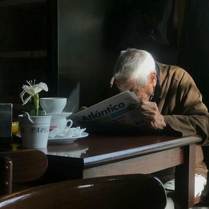 Elderly man reading a newspaper at a wooden table, showcasing cool and stylish grandparents in casual attire.