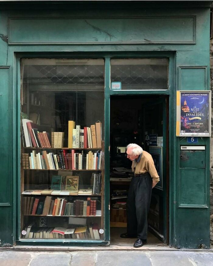 Elderly man showcasing cool and stylish grandparents fashion outside a vintage bookstore with green facade and shelves of books.
