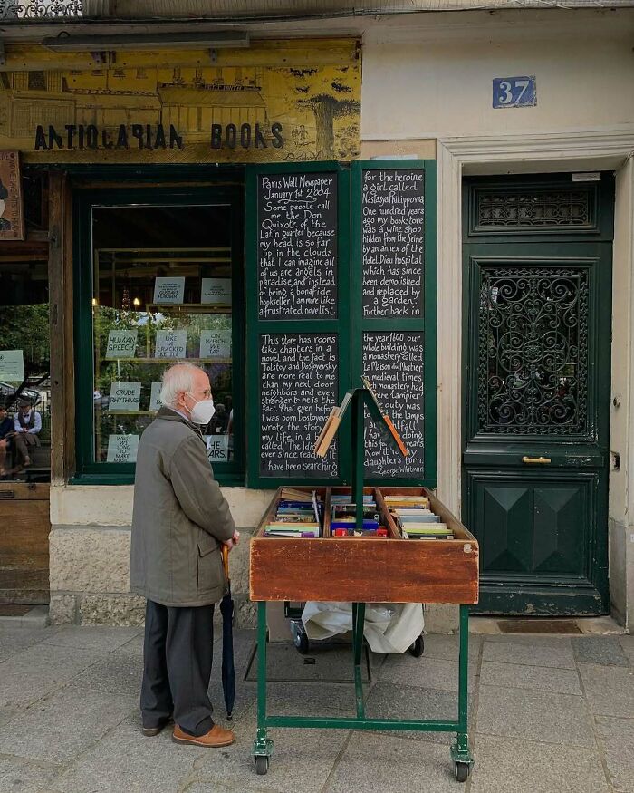 Elderly man in a cool and stylish outfit browsing books outside an antiquarian bookshop on a city street.