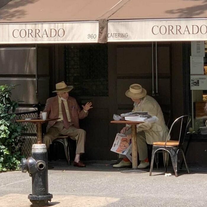 Two stylish grandparents wearing hats and suits, sitting outside a café, showcasing cool and fashionable outfits.