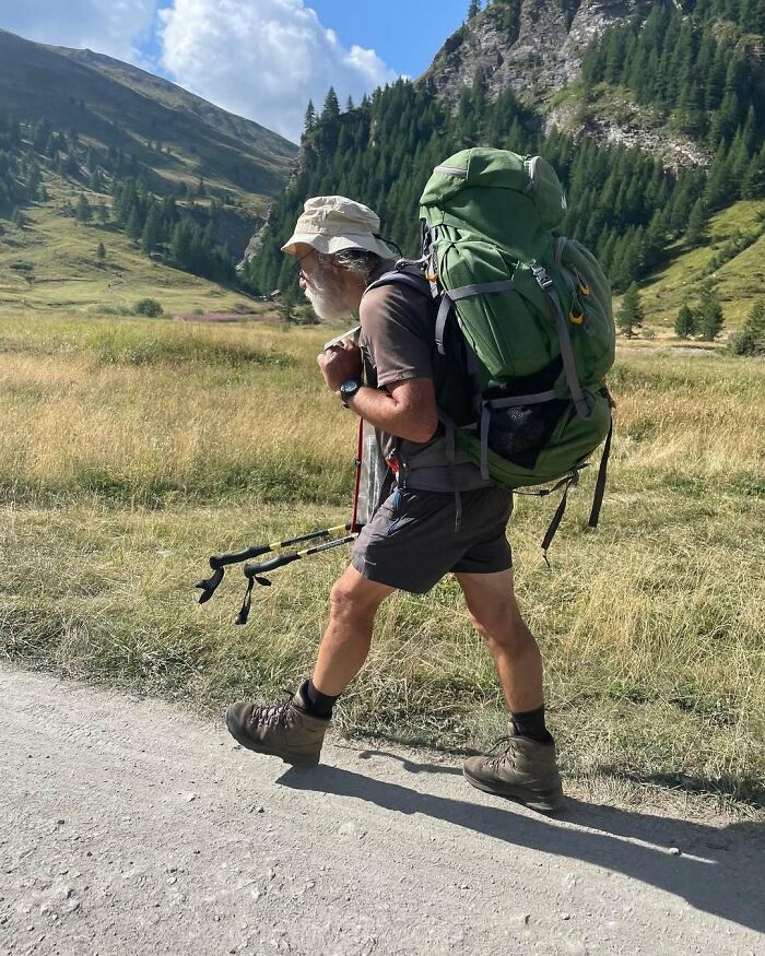 Active grandparent hiking in stylish outdoor gear with large green backpack in a scenic mountainous landscape.