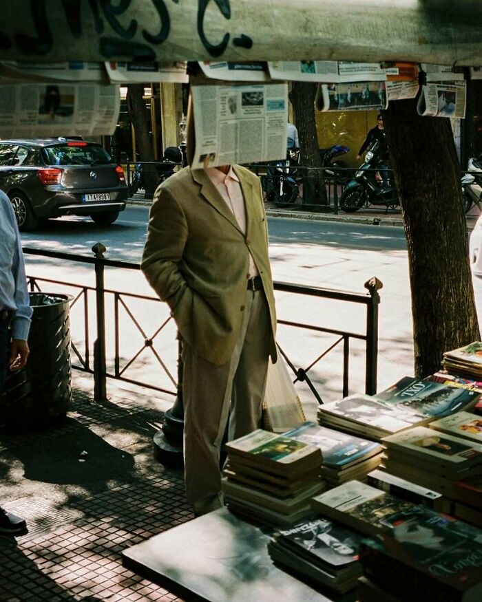 Stylish grandparent in beige suit browsing books at outdoor market under hanging newspapers on a sunny day.
