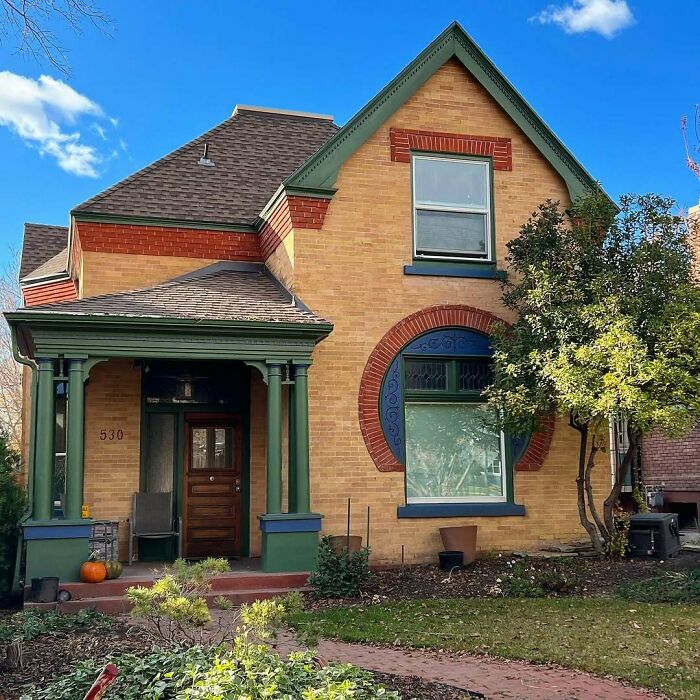 Charming old home with brick exterior, green trim, and a cozy front porch surrounded by trees and garden landscaping.
