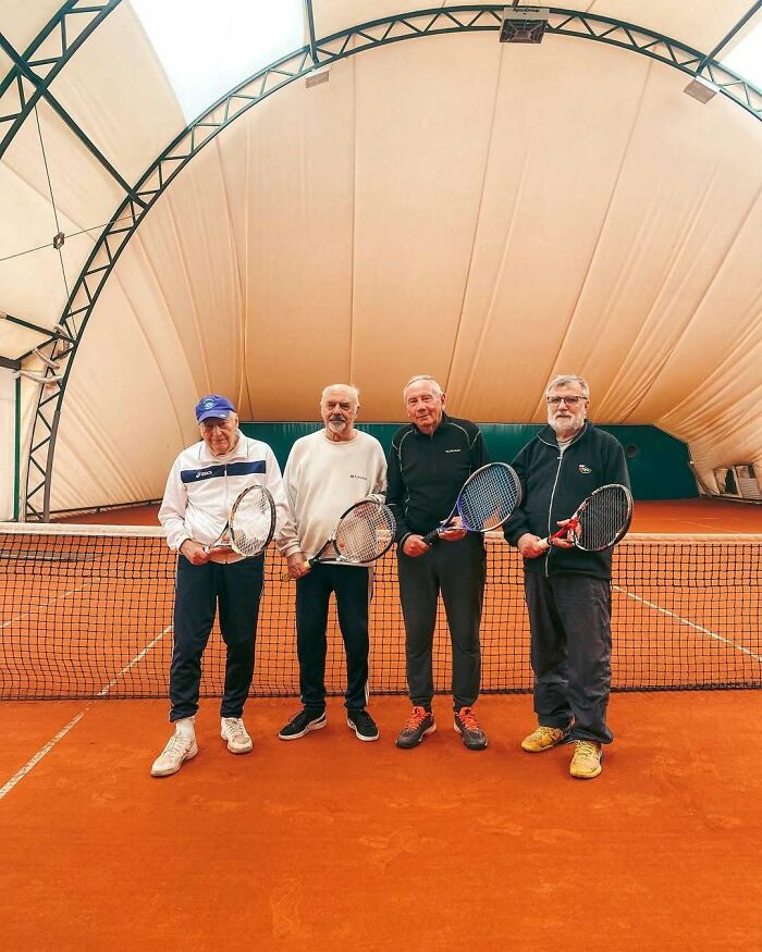 Four cool and stylish grandparents posing with tennis rackets on an indoor clay court, dressed in sporty outfits.