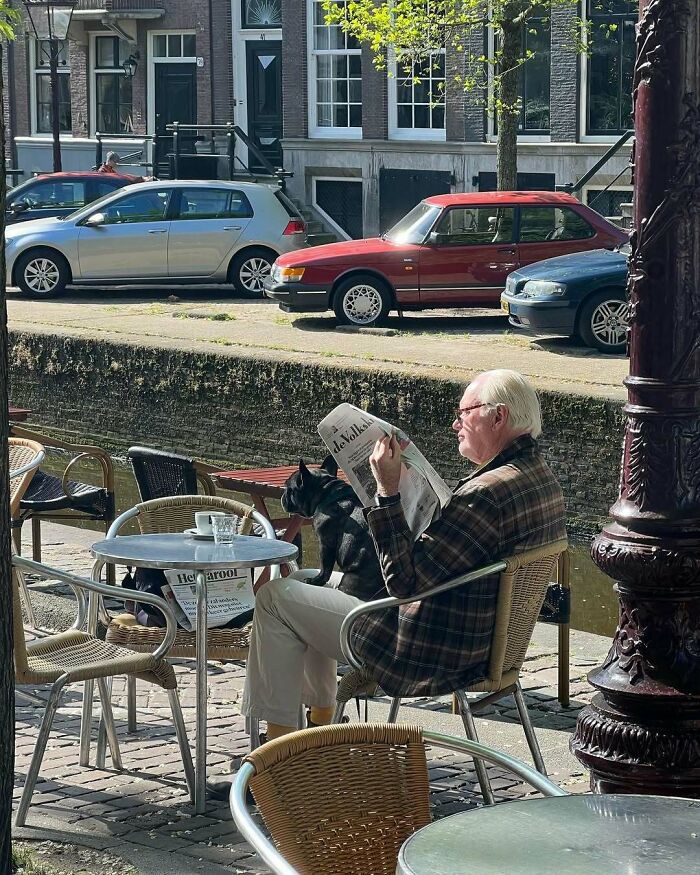 Elderly man in a stylish plaid jacket reading newspaper at outdoor cafe, showcasing cool and stylish grandparents fashion.