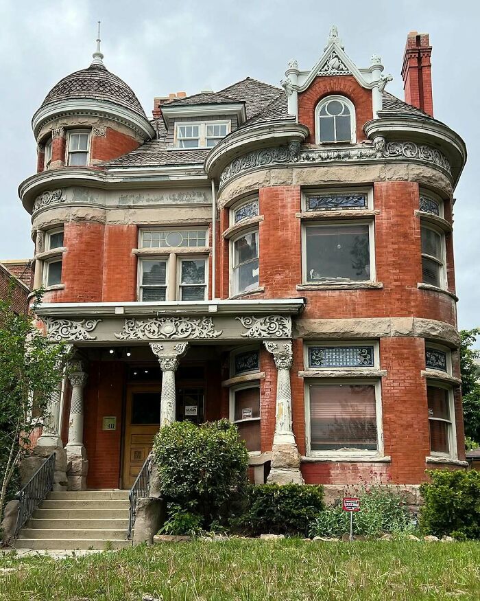 Victorian-style adorable and lovely old home with red brick, ornate columns, and turret under a cloudy sky.