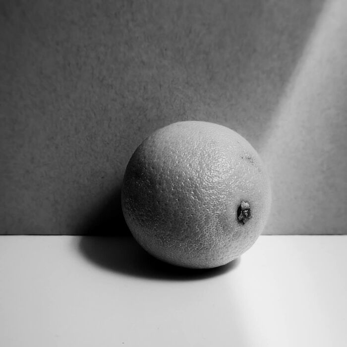 Black-and-white photo of a single textured orange with dramatic lighting and shadows, capturing detail and contrast.