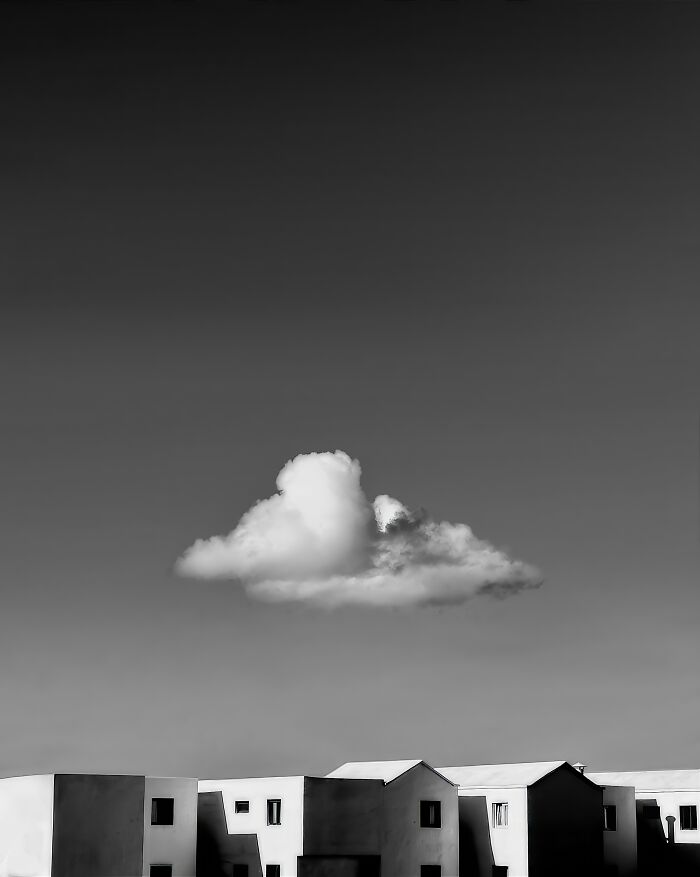 Single fluffy cloud floating above minimalist buildings in a black-and-white photo from Exposure One Awards 2025.