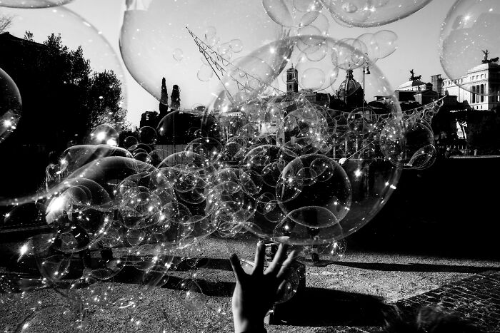 Black-and-white photo of a hand reaching towards floating bubbles in a cityscape, captured for Exposure One Awards.
