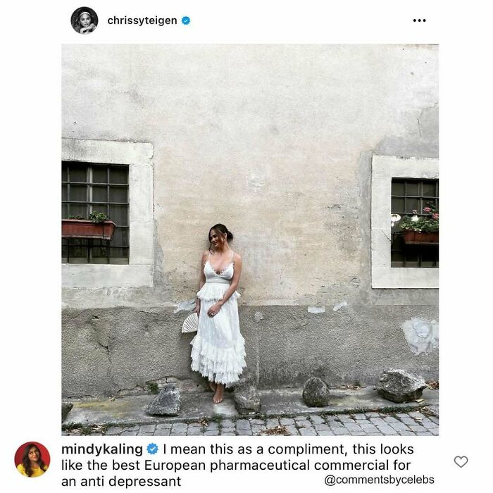 Chrissy Teigen in a white dress leaning against a rustic wall, an example of celebs dropping unexpected gems in comments.