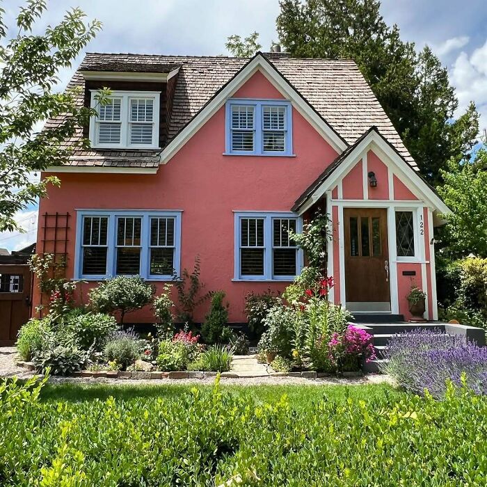 Charming old home with pink exterior, blue window frames, and a lush garden, showcasing lovable and adorable vintage appeal.