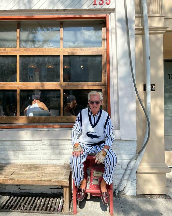 Stylish grandfather wearing striped outfit and vest, seated outside a cafe, showcasing cool fashion for grandparents.