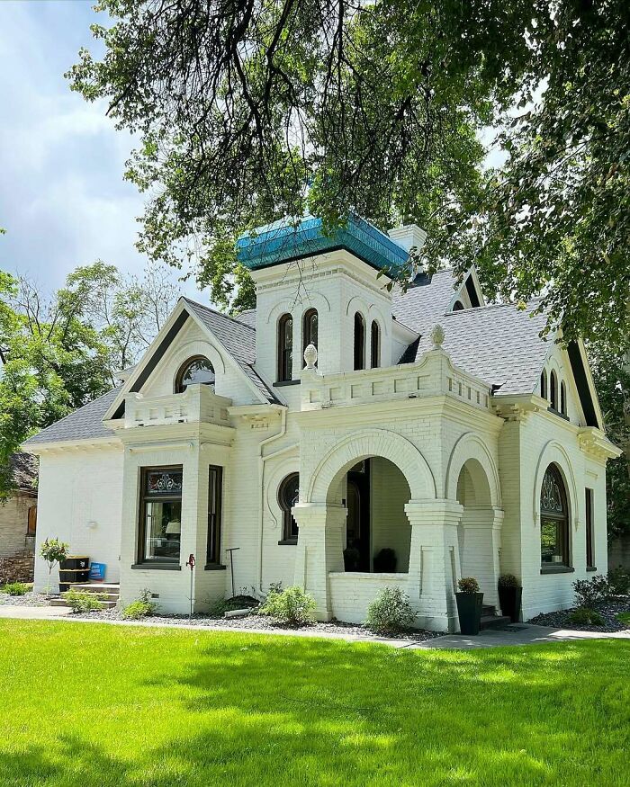 Victorian-style old home with white brick exterior, arched entryway, surrounded by lush green lawn and trees.