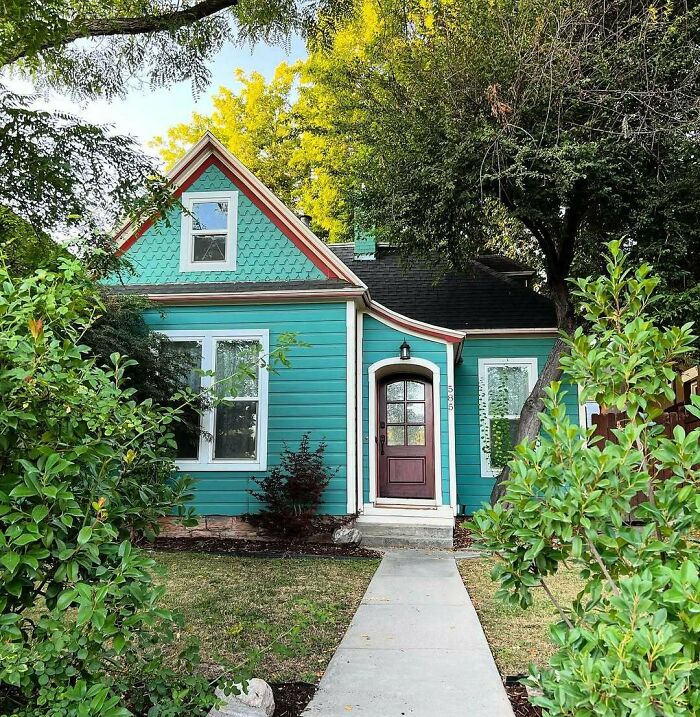 Charming old home with teal siding, surrounded by lush greenery, inviting and adorable for a cozy lifestyle.