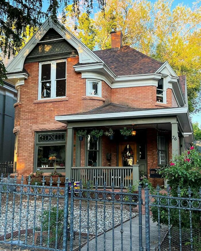 Charming old brick home with a porch and iron fence surrounded by greenery, perfect for lovers of lovely old homes.
