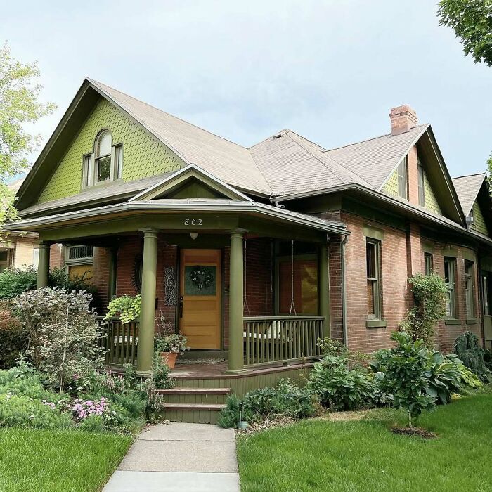 Charming old home with green accents, a cozy front porch, and lush garden, perfect for lovers of lovely old homes.