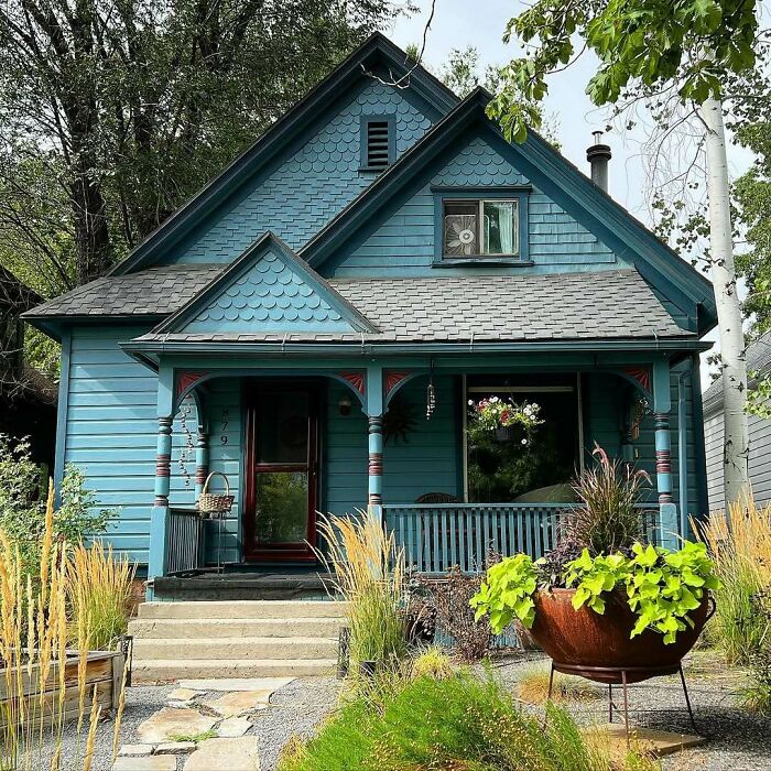 Charming blue old home with a front porch, surrounded by greenery and decorative plants in the garden.