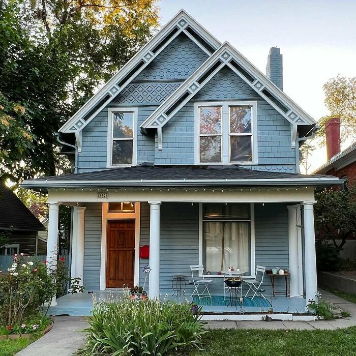 Charming old home with blue siding, decorative gables, and a cozy front porch featuring white columns and outdoor seating.