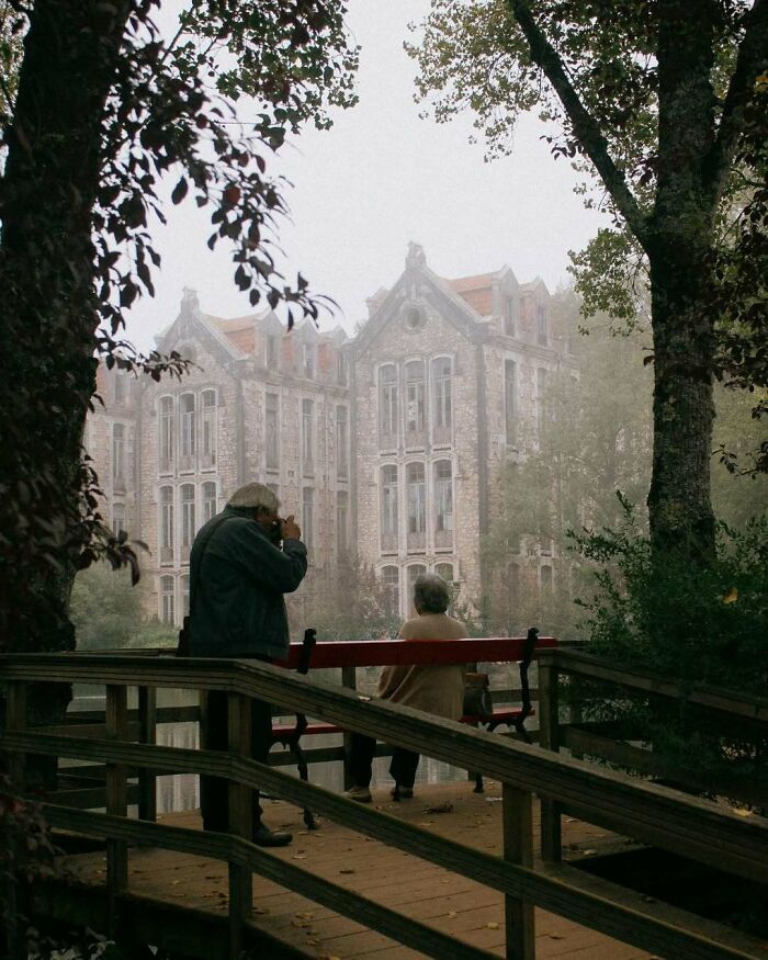 Stylish grandparents enjoying a foggy day near a historic building, with one grandparent photographing the scene.