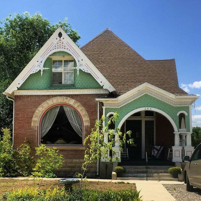 Charming old home with green accents, decorative trim, and a cozy front porch surrounded by greenery on a sunny day.
