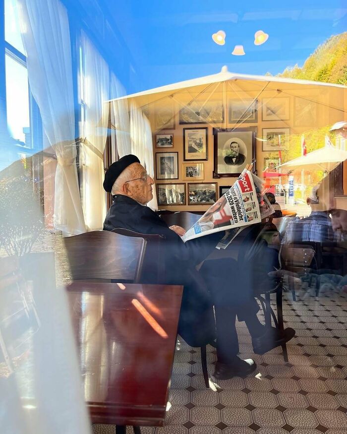 Elderly man wearing a black beret and glasses, reading a newspaper in a cozy cafe, showcasing cool and stylish grandparents.