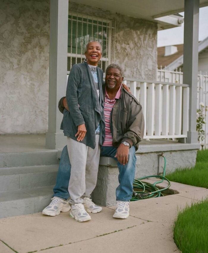 Stylish grandparents wearing casual outfits and sneakers, posing happily outside a home on a porch step.