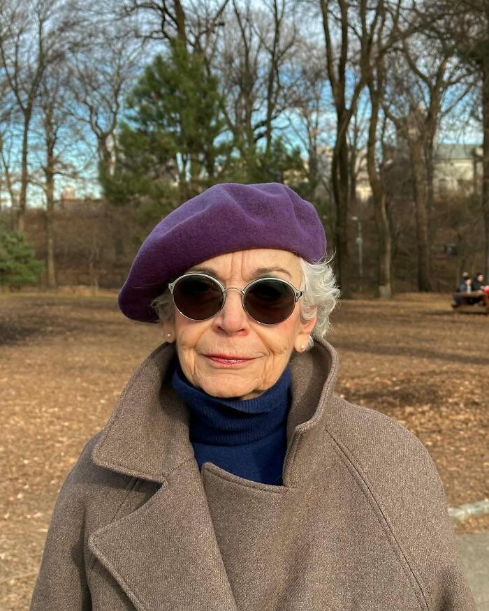 Stylish grandparent wearing a purple beret, round sunglasses, and a brown coat, showcasing cool and fashionable outfit outdoors.