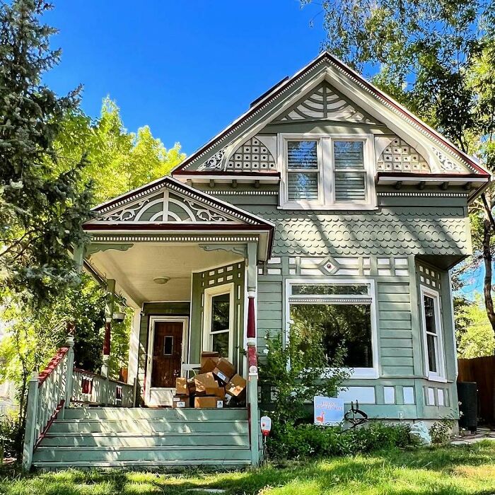 Adorable old home with detailed trim, green exterior, and a porch surrounded by trees on a sunny day.