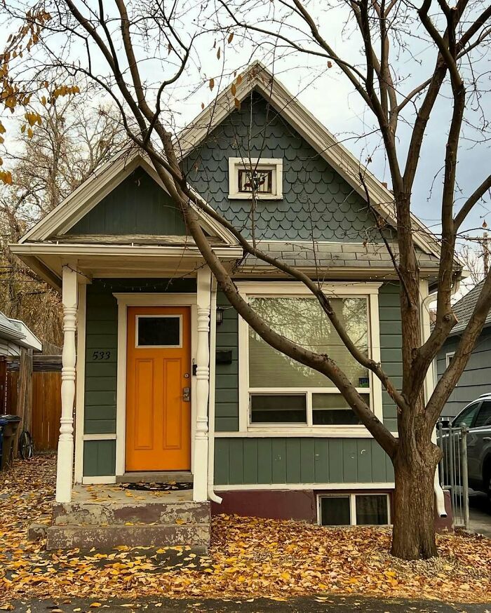 Charming old home with green siding, orange door, and autumn leaves covering the yard, showcasing lovely old homes appeal.