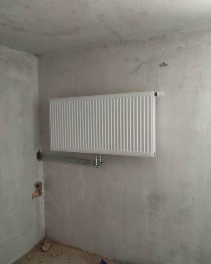Radiator mounted unusually high on wall with pipes awkwardly bent in a poorly executed construction design.