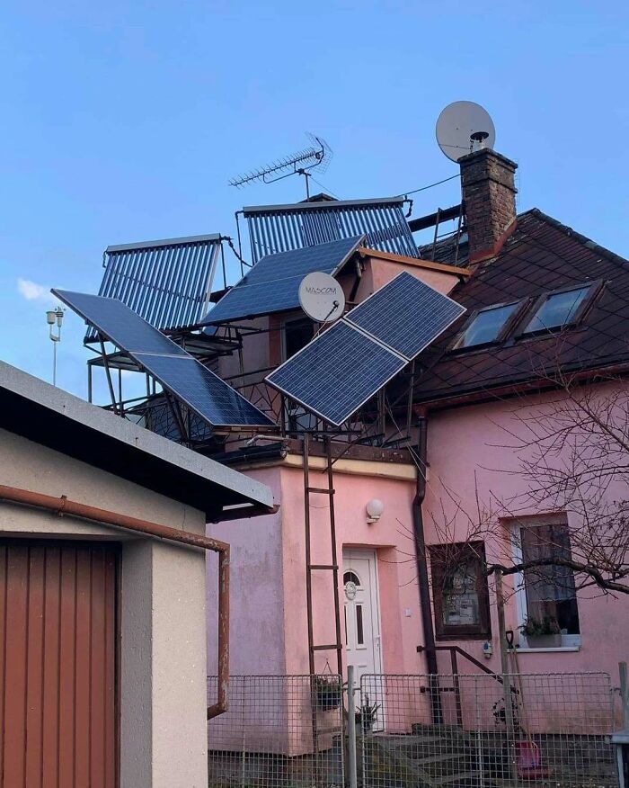 Unusual construction design with multiple solar panels and antennas awkwardly installed on a residential roof.