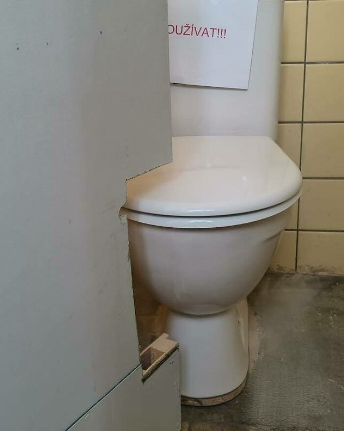 Toilet installed behind a wall with an impractical cutout, showing a flawed construction and design mistake.