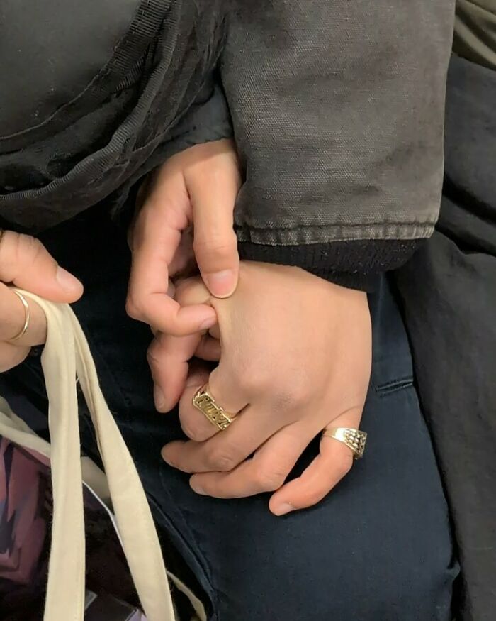 Close-up of people on the New York subway holding hands and carrying a tote bag with rings on fingers.