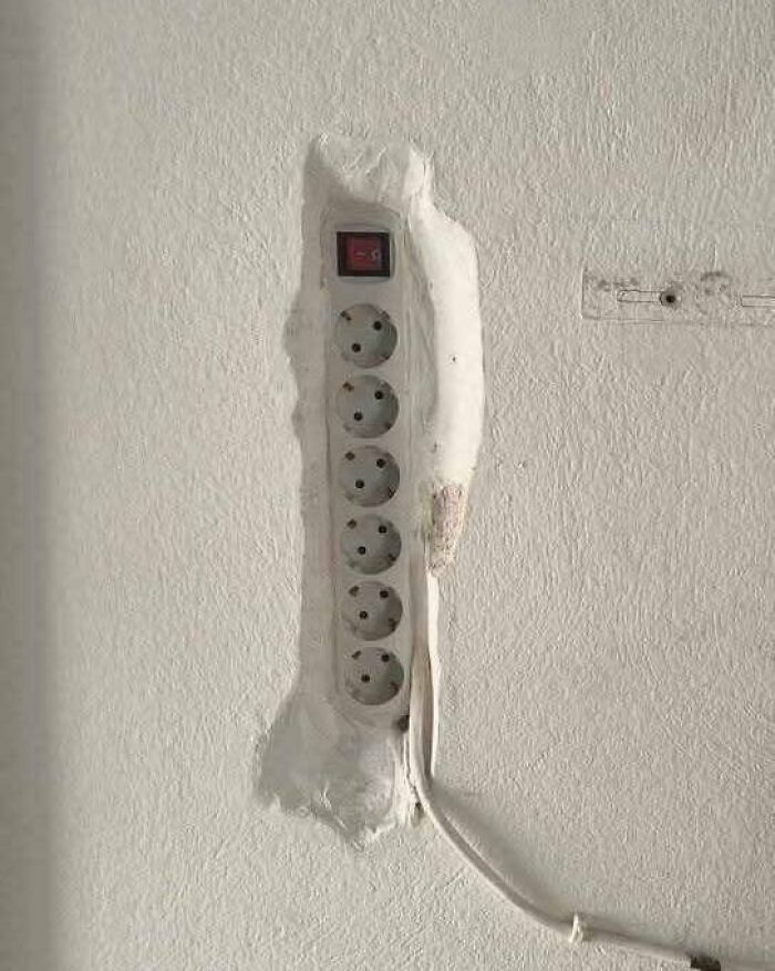 Power strip installation poorly embedded in wall with rough plaster, showing flawed construction and design.