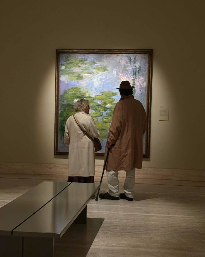 Two stylish grandparents in classic coats admiring artwork in a gallery, showcasing cool and fashionable outfits.