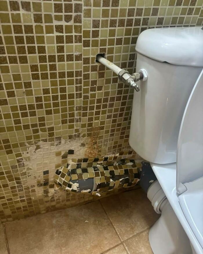 Toilet plumbing with poorly tiled wall and pipe covered in mismatched tiles showing bad construction and design work.