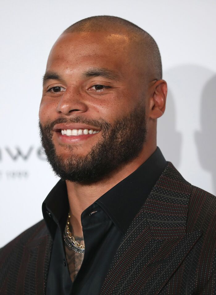 Close-up of a smiling highest paid athlete of 2025 wearing a dark suit and gold chain at a formal event.