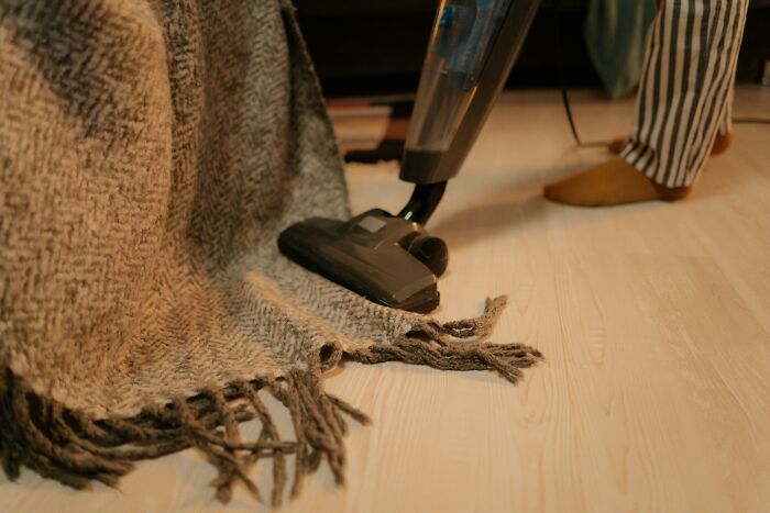 Person vacuuming a fringed blanket on a wooden floor, illustrating where do you draw the line deal breakers.