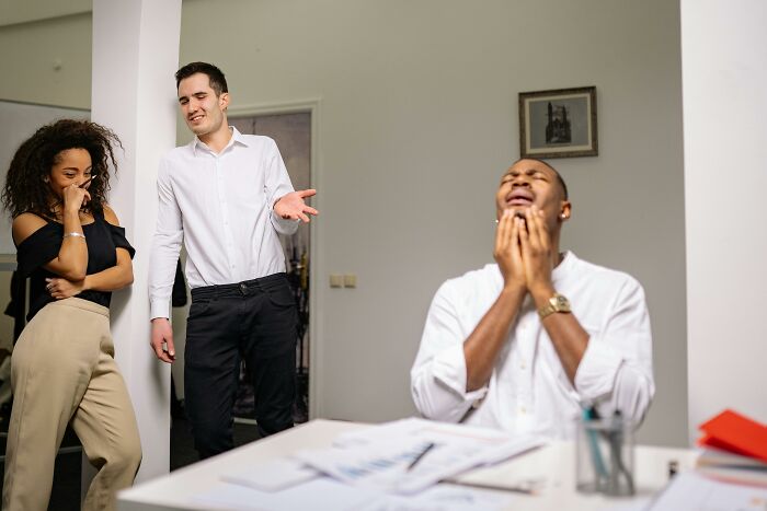 Three coworkers in office dealing with tricky deal breakers, showing frustration and awkward interaction during discussion.