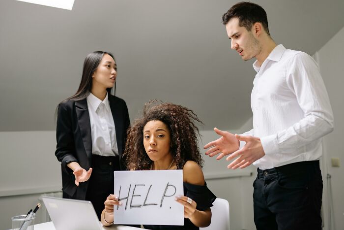 Three coworkers having a tense discussion while a woman holds a help sign, illustrating tricky deal breakers at work.