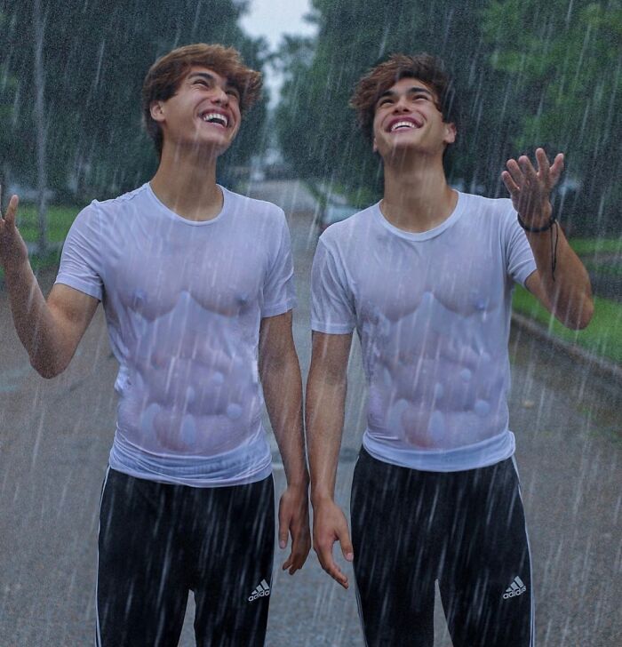 Two influencers wearing wet white shirts and black Adidas pants, smiling and enjoying the rain outdoors.