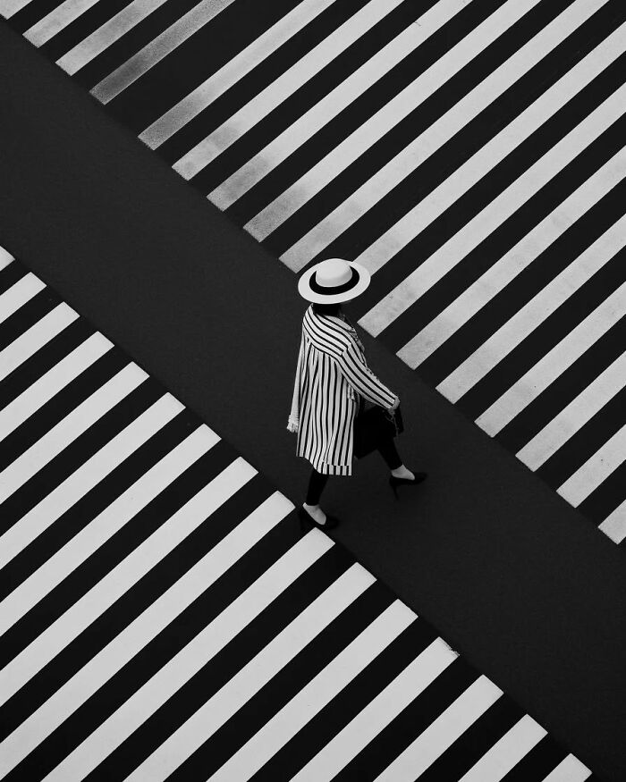 Person in striped outfit crossing a minimalist black and white striped pedestrian crosswalk in a peaceful escape setting.