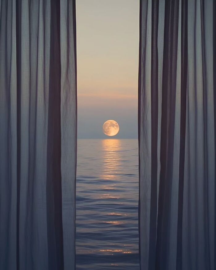 Minimalist photo of a full moon rising over calm ocean waters, framed by sheer curtains at twilight, evoking a peaceful escape.