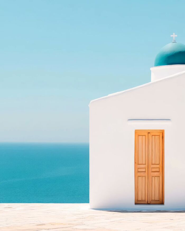 Minimalist photo of a white building with a blue dome and wooden door overlooking a calm turquoise sea.