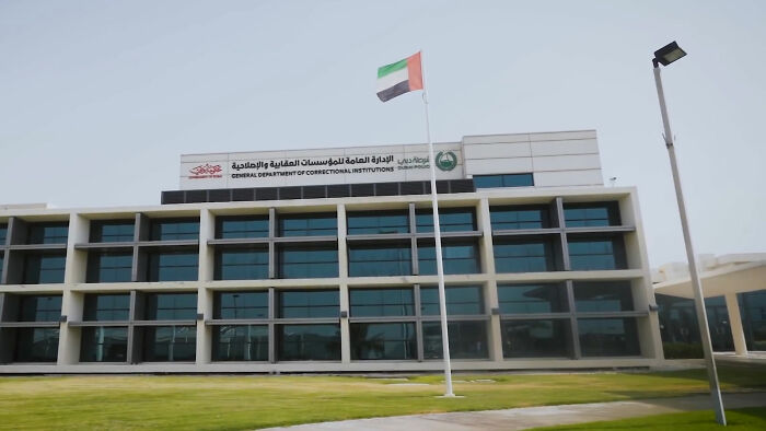 Dubai prison exterior with flag, representing the harsh sentence of a glamorous law student in a high-security facility.