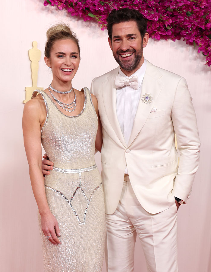 Emily Blunt posing in a shimmering dress with a braless look, sparking plastic surgery rumors at an event.