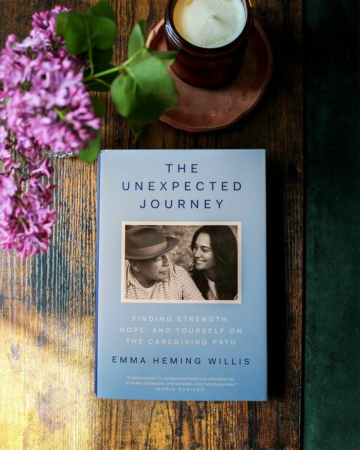 Book titled The Unexpected Journey by Emma Heming Willis about caregiving and dementia, next to a candle and purple flowers on a wooden table Book titled The Unexpected Journey by Emma Heming Willis about caregiving and dementia, next to a candle and purple flowers on a wooden table