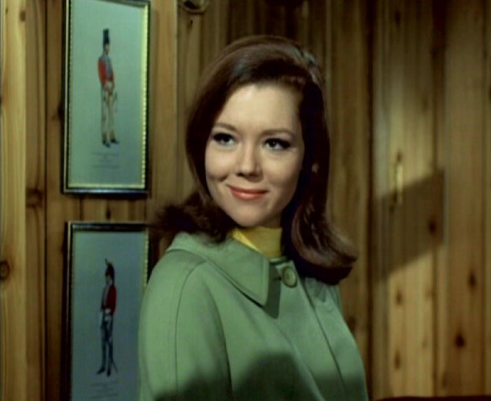 Young woman in a green coat smiling indoors, representing well-written female characters in movies breaking stereotypes.